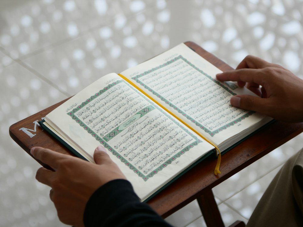 Hands resting on an open mushaf in soft daylight